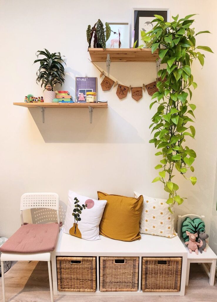 Foto van de inrichting van de praktijk. We zien een zitbankje met kussens, enkele wandplanken met decoratie en planten.